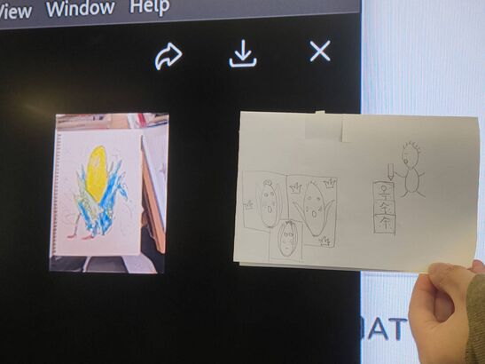 Picture of a drawing held in front of a monitor. Both drawing and monitor display a drawing of a corn with cartoon vibes.