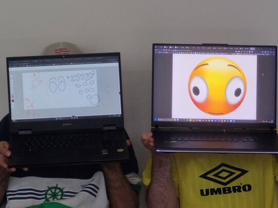 Two people posing with laptops covering their face. On the displays funny emojis