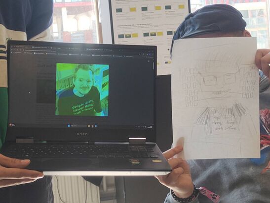 Two people posing with a drawing and a laptop, showcasing an old profile picture.