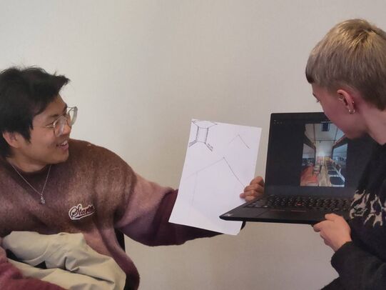 Two people posing with a laptop and drawing to display results of an excercise. Photo quality is terrible, and the drawing not really legible.