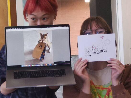 Two people posing with a laptop and a drawing, both displaying a cat related picture.