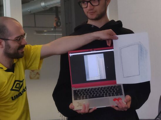 Two people posing with a laptop and a drawing of a big cubic white building